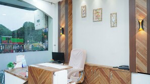 A reception desk with a computer, a chair, and a window with a view of a train. - Hotel Pleasure (Ujjain)