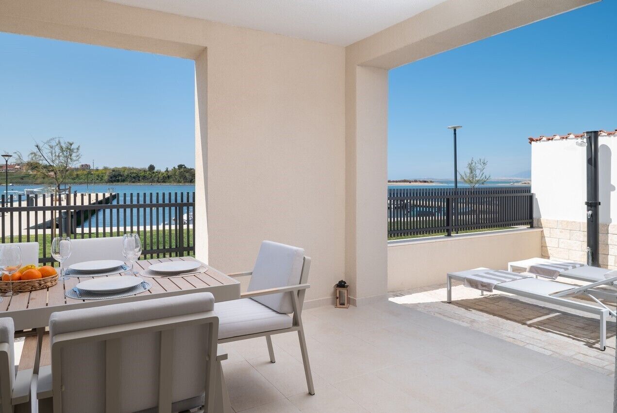 Eine Terrasse mit Esstisch, weißen Stühlen und Meerblick.