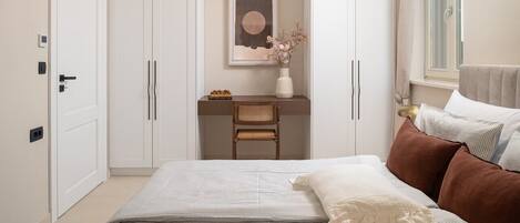 Un dormitorio con cama, mesita de noche, silla, estante con objetos decorativos y ventana con cortinas.