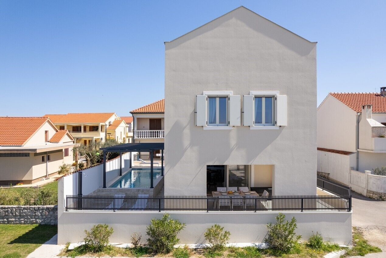 A modern two-story building with a swimming pool, a covered patio, and a balcony.