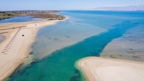An aerial view of a coastal area with clear blue waters, sandy beaches, and a few structures.
