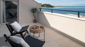 A balcony with two black lounge chairs, a small round table with drinks, a potted plant, and a view of the sea and beach.