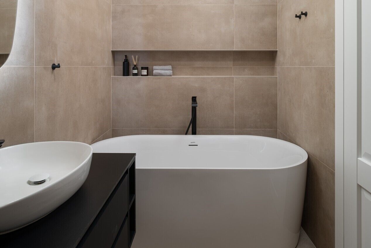 A modern bathroom with a freestanding bathtub, a round sink, and a built-in shelf with toiletries.
