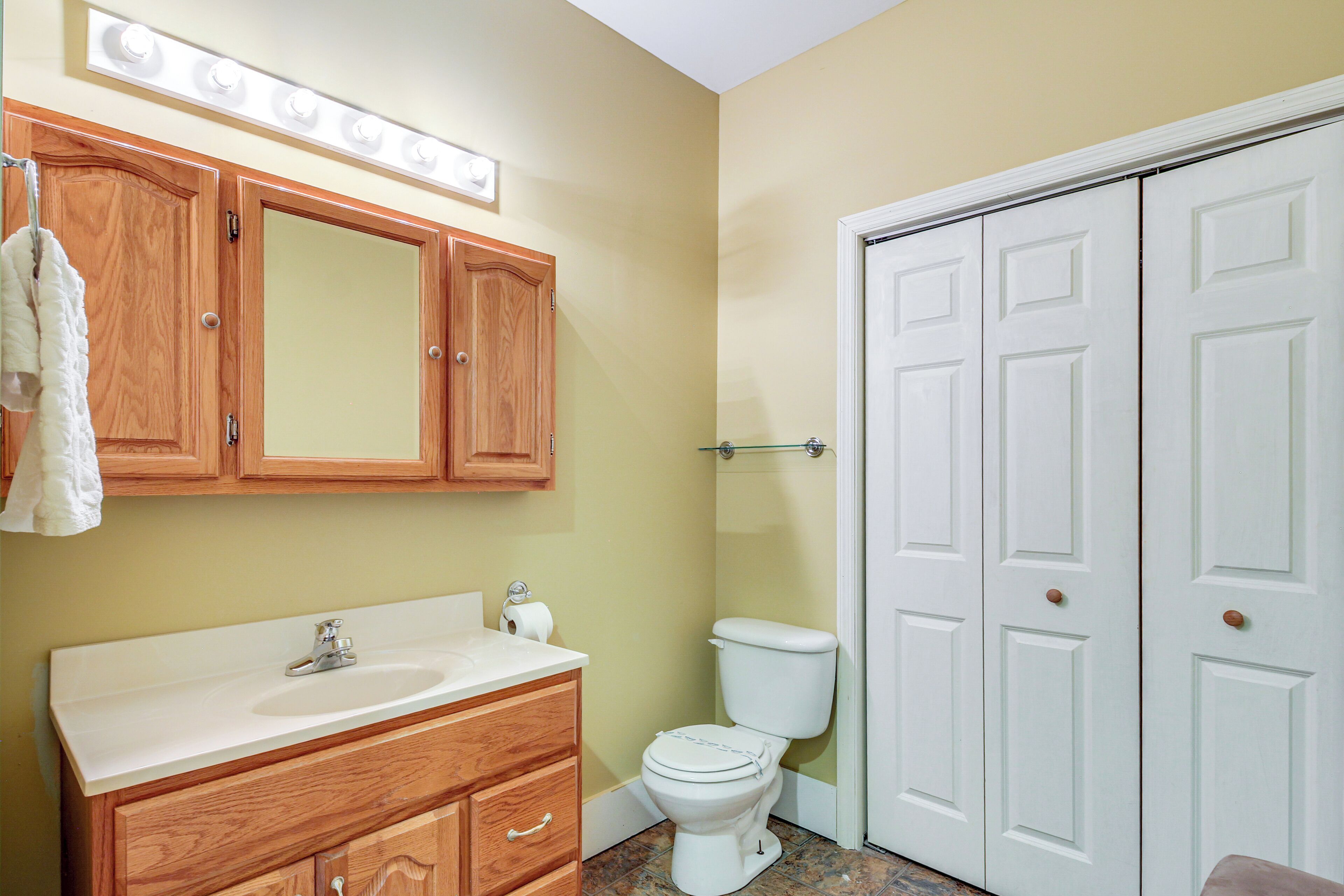 Un baño con armarios de madera, un lavabo blanco, un inodoro y una puerta blanca.
