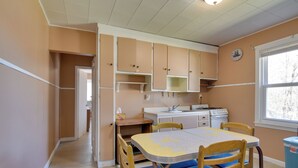 A kitchen with wooden cabinets, a dining table with chairs, a window with blinds, and a clock on the wall. - Shared Lake Access & Fire Pit: Catskills Getaway! (Ellenville)