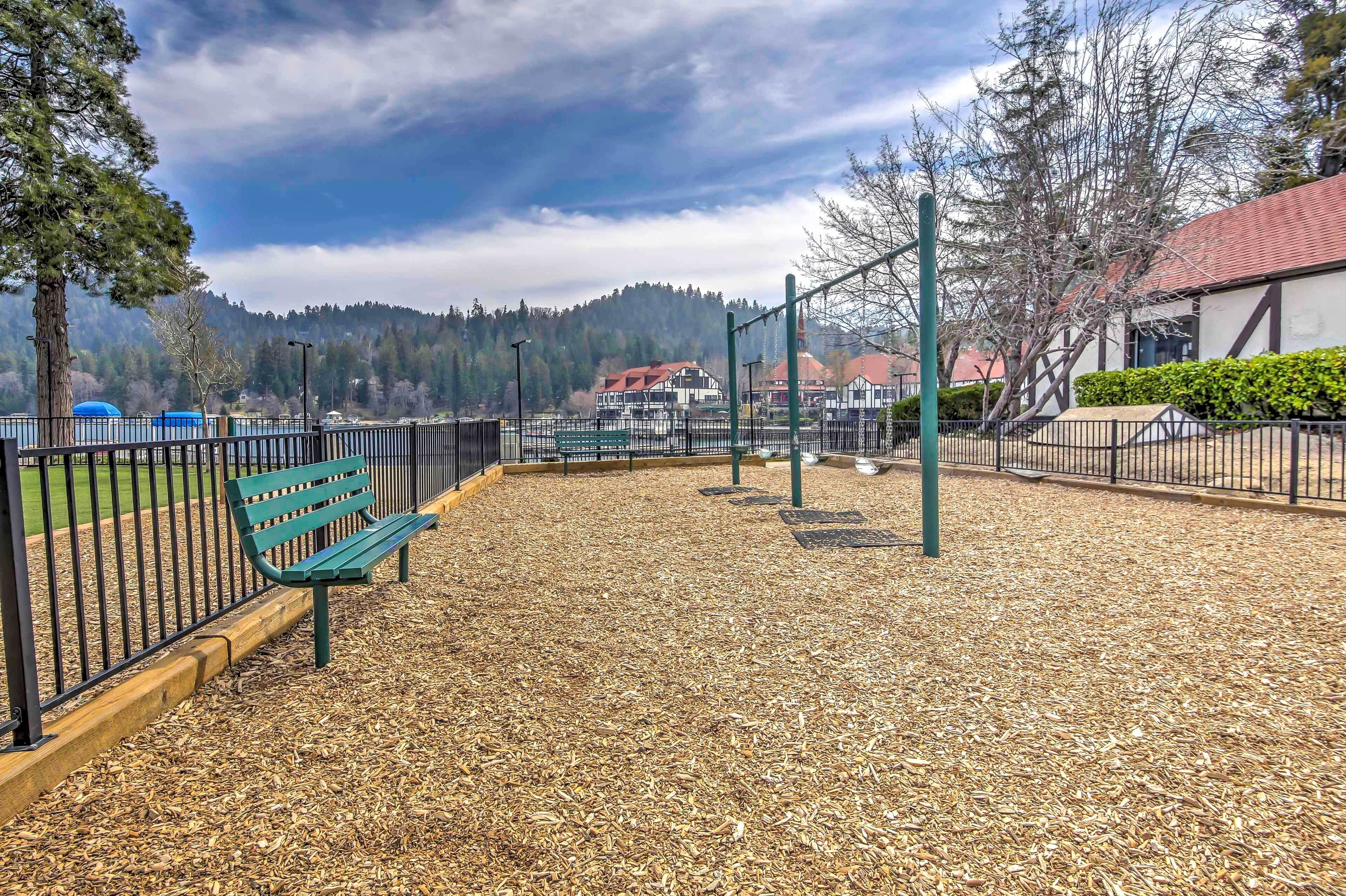 A playground with a green bench, metal play structures, and a fence.