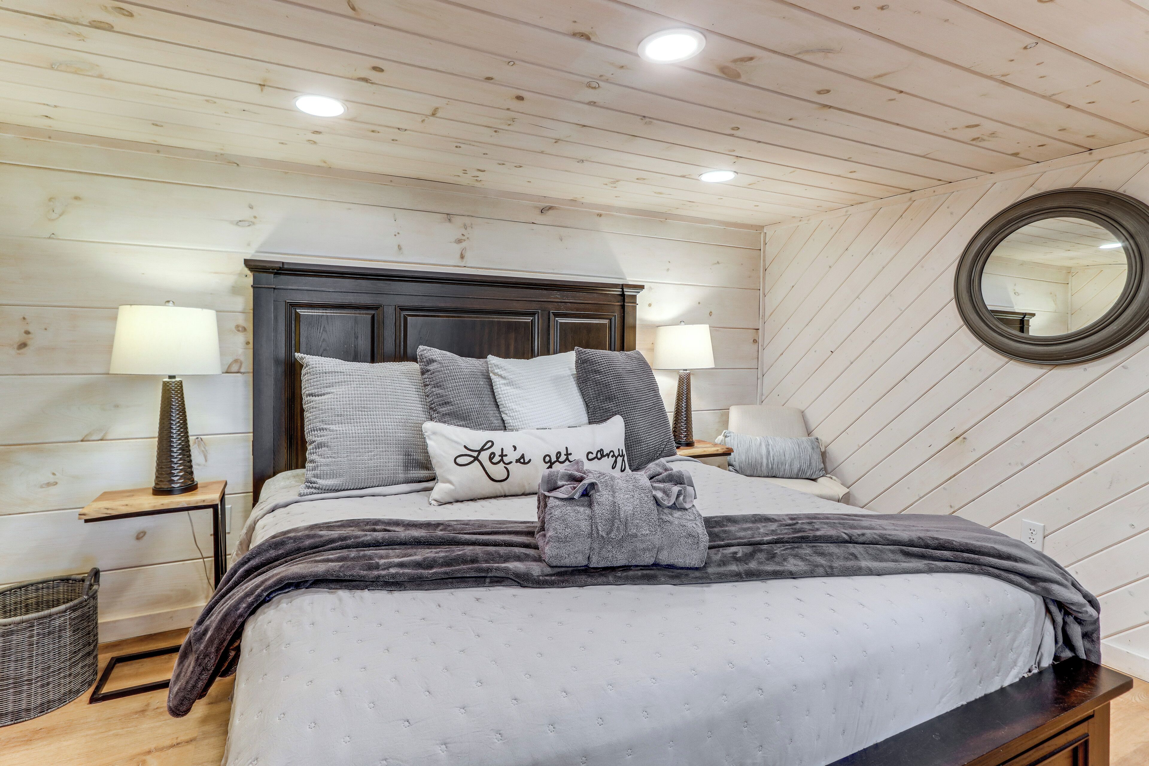 A neatly made bed with a headboard, two bedside tables with lamps, a round mirror on the wall, and a basket on the floor.
