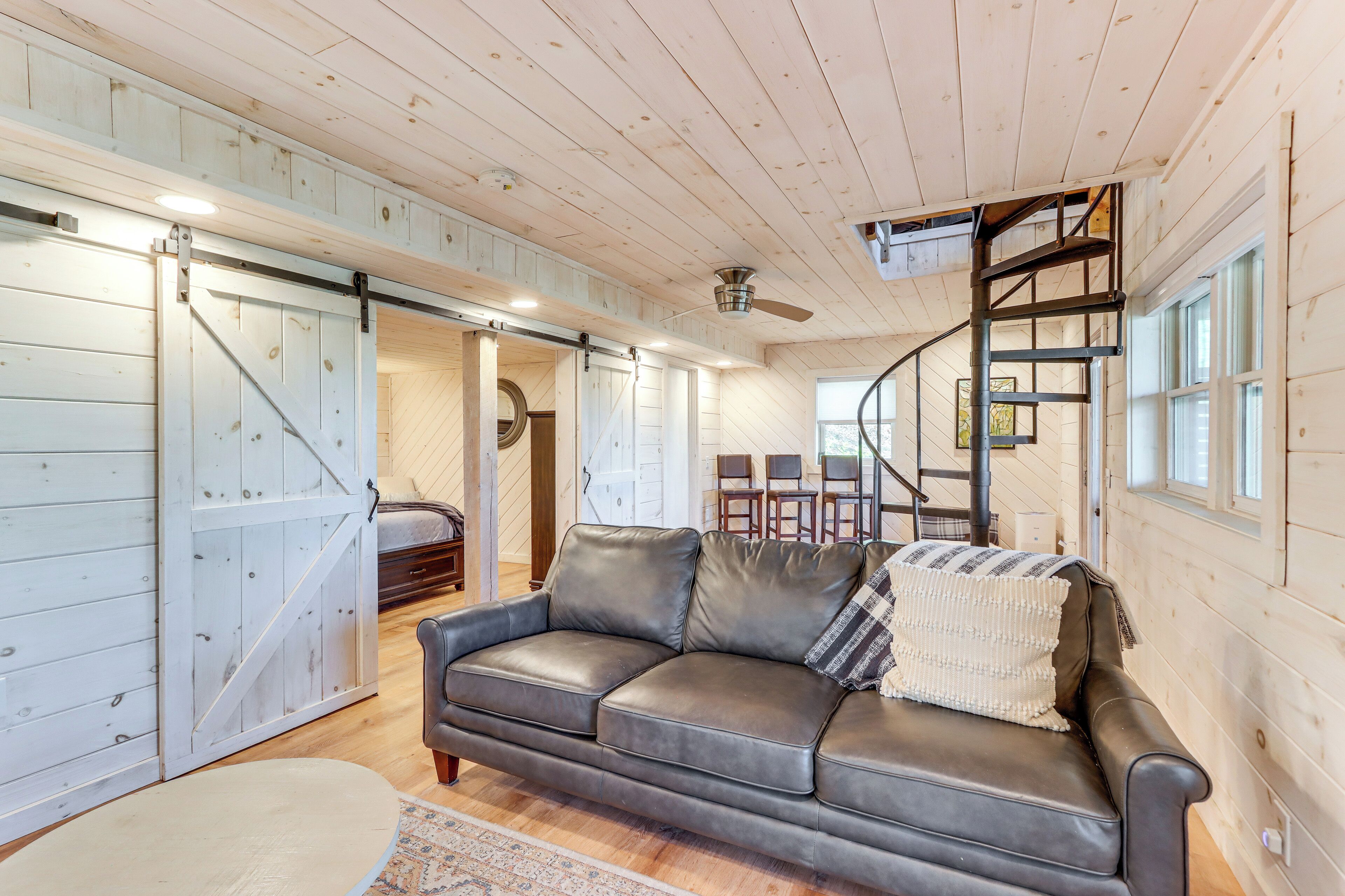 A cozy living room with a leather sofa, a wooden ceiling, and a spiral staircase.