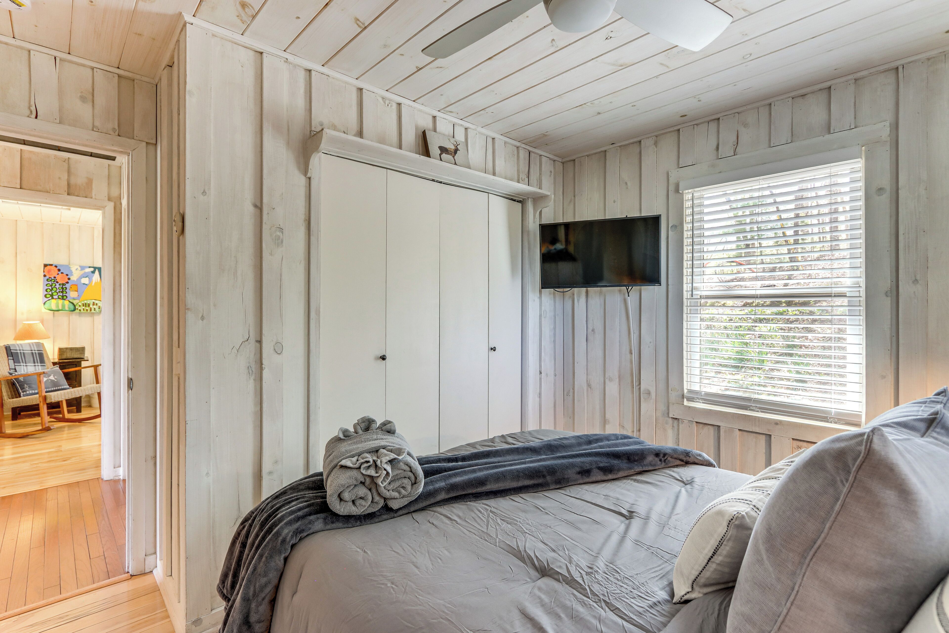 Une chambre à coucher comprenant un lit, un téléviseur, une fenêtre avec des stores et une porte donnant sur une autre pièce.