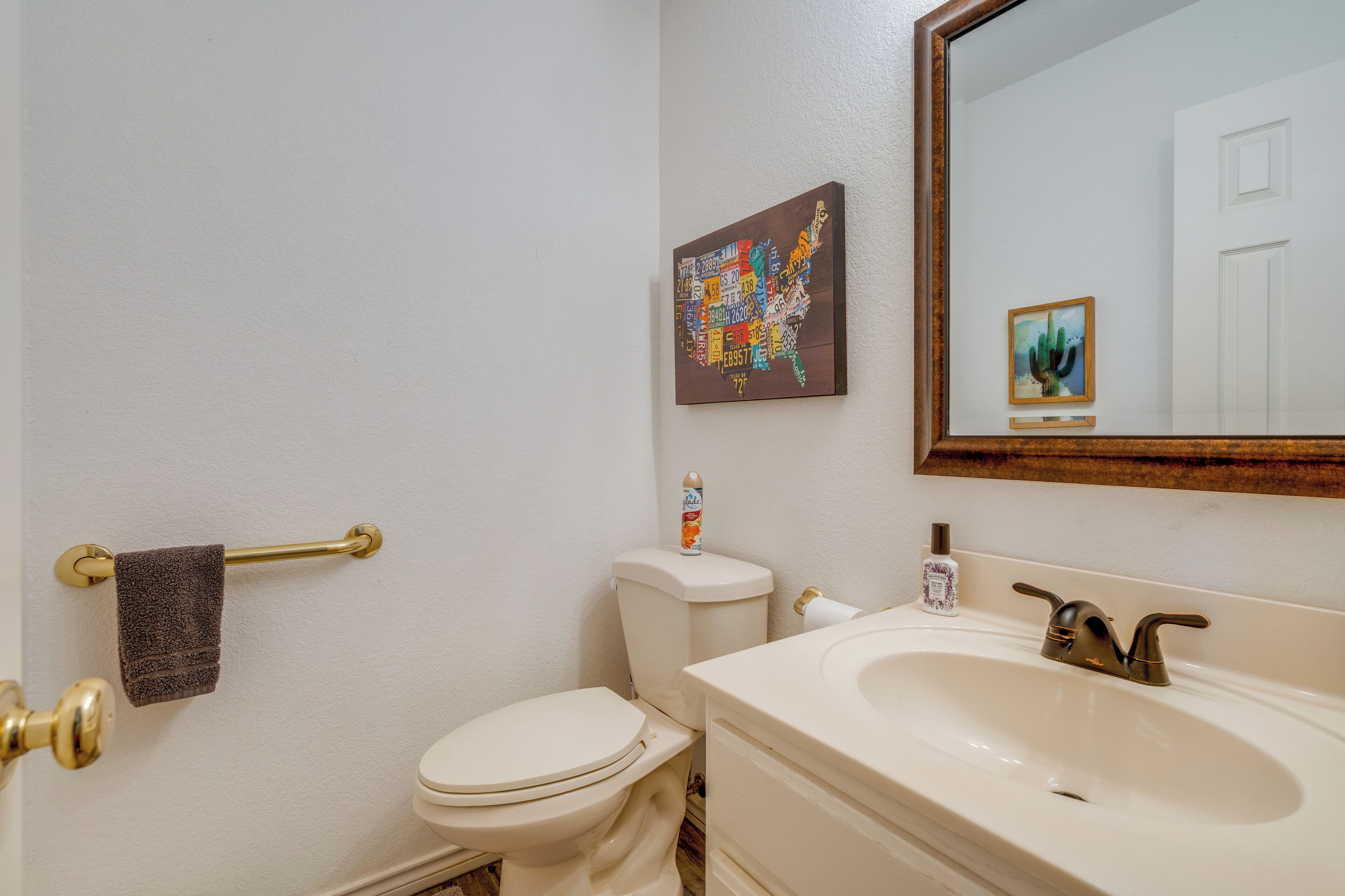 A bathroom with a white toilet, a sink with a gold faucet, a towel rack, and a map of the United States on the wall.