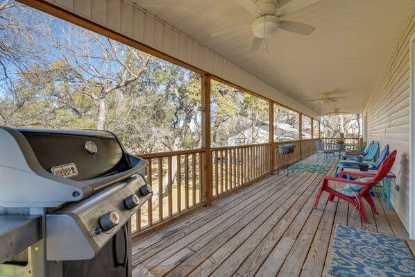 A covered porch with a grill, outdoor furniture, and a view of trees.
