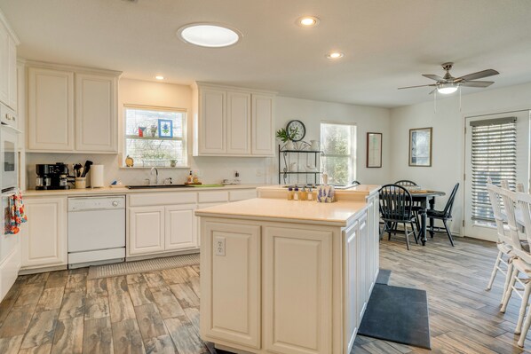 A kitchen with white cabinets, a dishwasher, a dining area with a table and chairs, and a ceiling fan.
