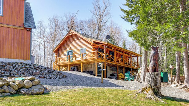 A log cabin with a porch, a stone wall, and a large tree trunk. - Waterfront Anglers Oasis in The Maine Highlands! (Carmel)