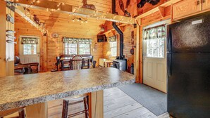A wooden cabin interior with a kitchen area featuring a granite countertop, bar stools, a refrigerator, and a dining table. - Waterfront Anglers Oasis in The Maine Highlands! (Carmel)