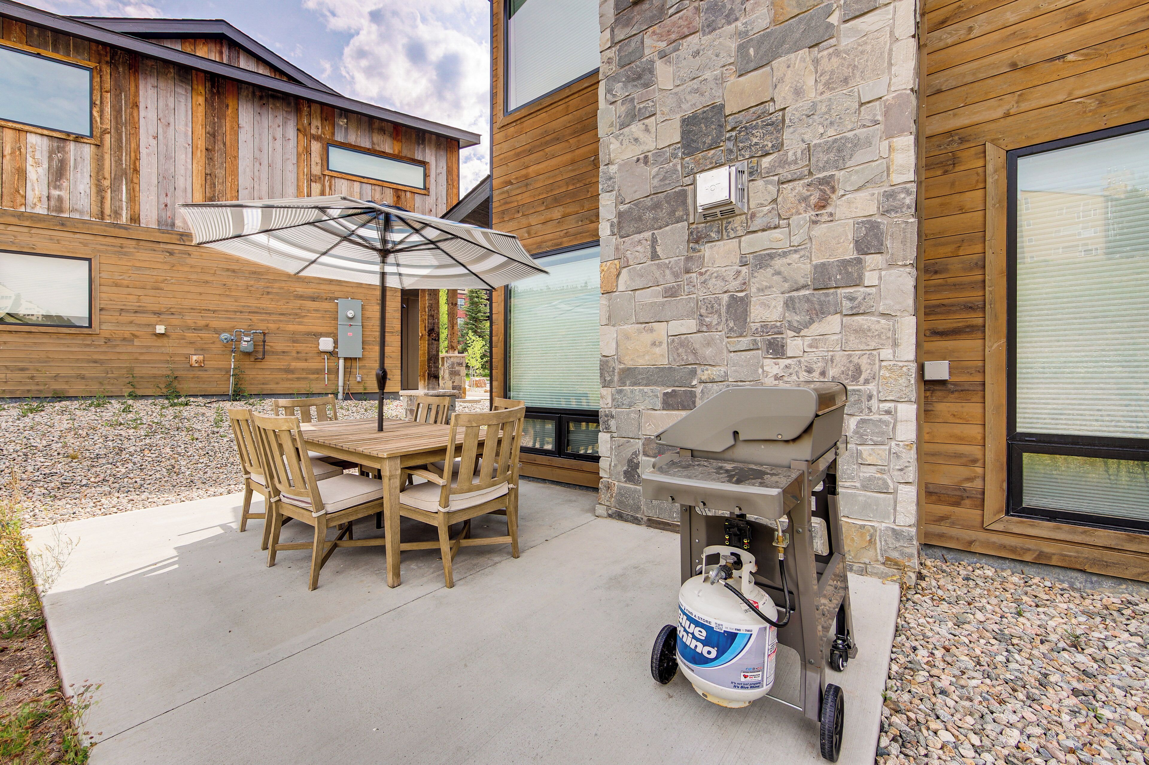 An outdoor patio with a wooden table and chairs, a grill, and a propane tank.