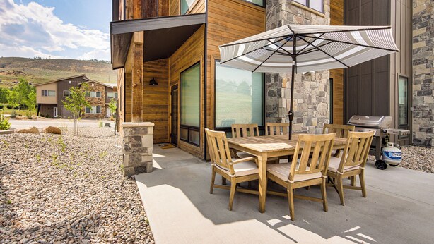 Un patio con tavolo e sedie in legno, un ombrellone e un barbecue.