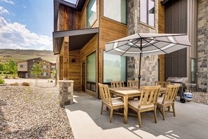 A patio with a wooden table and chairs, an umbrella, and a grill. - Walk to Ski Lift: Granby Ranch Family Retreat! (Granby)