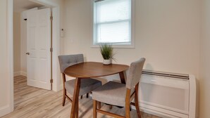 A dining area with a round wooden table, two grey upholstered chairs, a potted plant, and a white radiator. - 3 Mi to Main Street: Newly Renovated Wareham Apt! (Wareham)