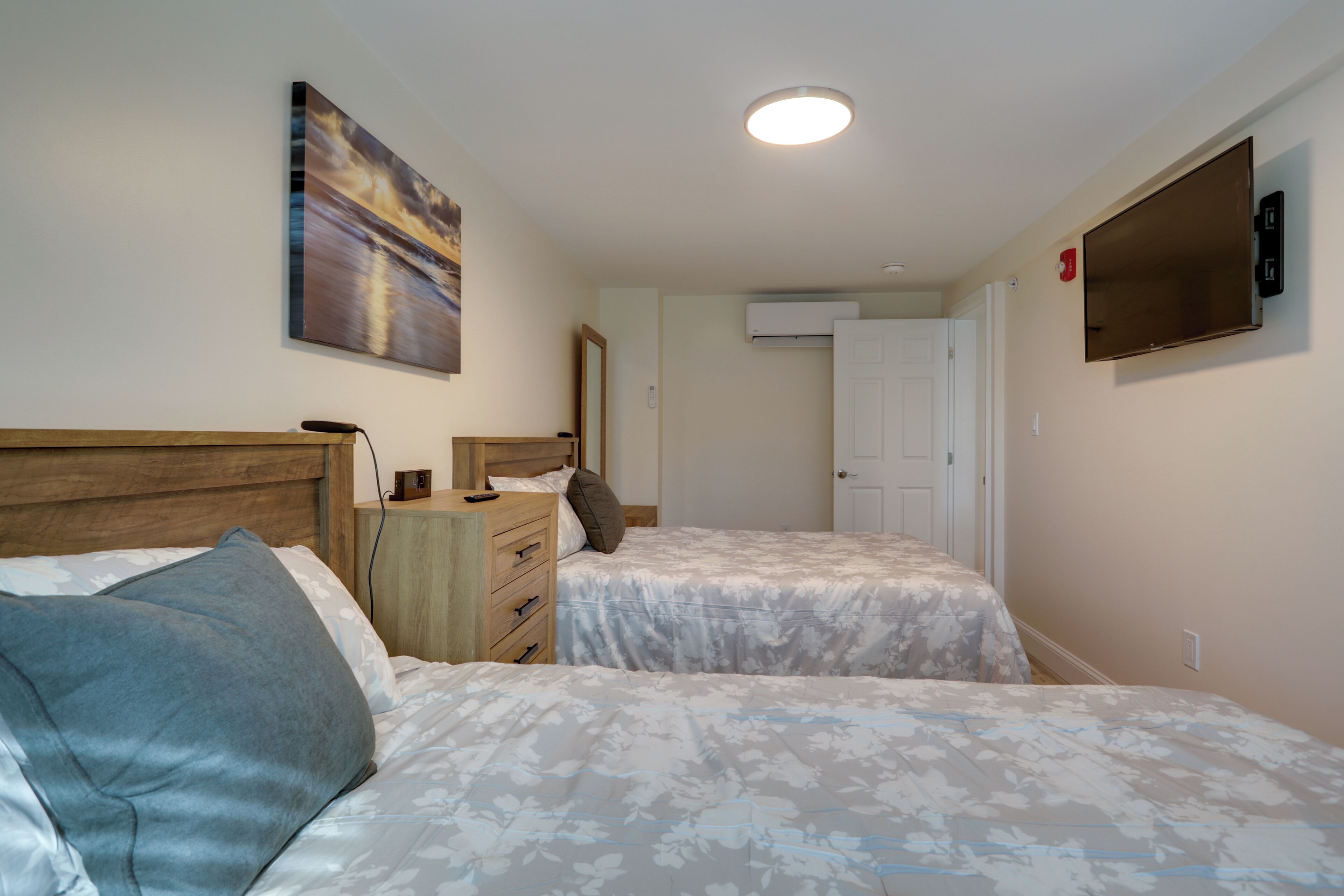 Une chambre avec deux lits, une commode, un tableau et un téléviseur fixé au mur.