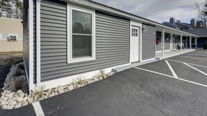 A single-story building with a grey exterior and white trim, featuring a covered porch area and a parking lot in front. - 3 Mi to Main Street: Newly Renovated Wareham Apt! (Wareham)