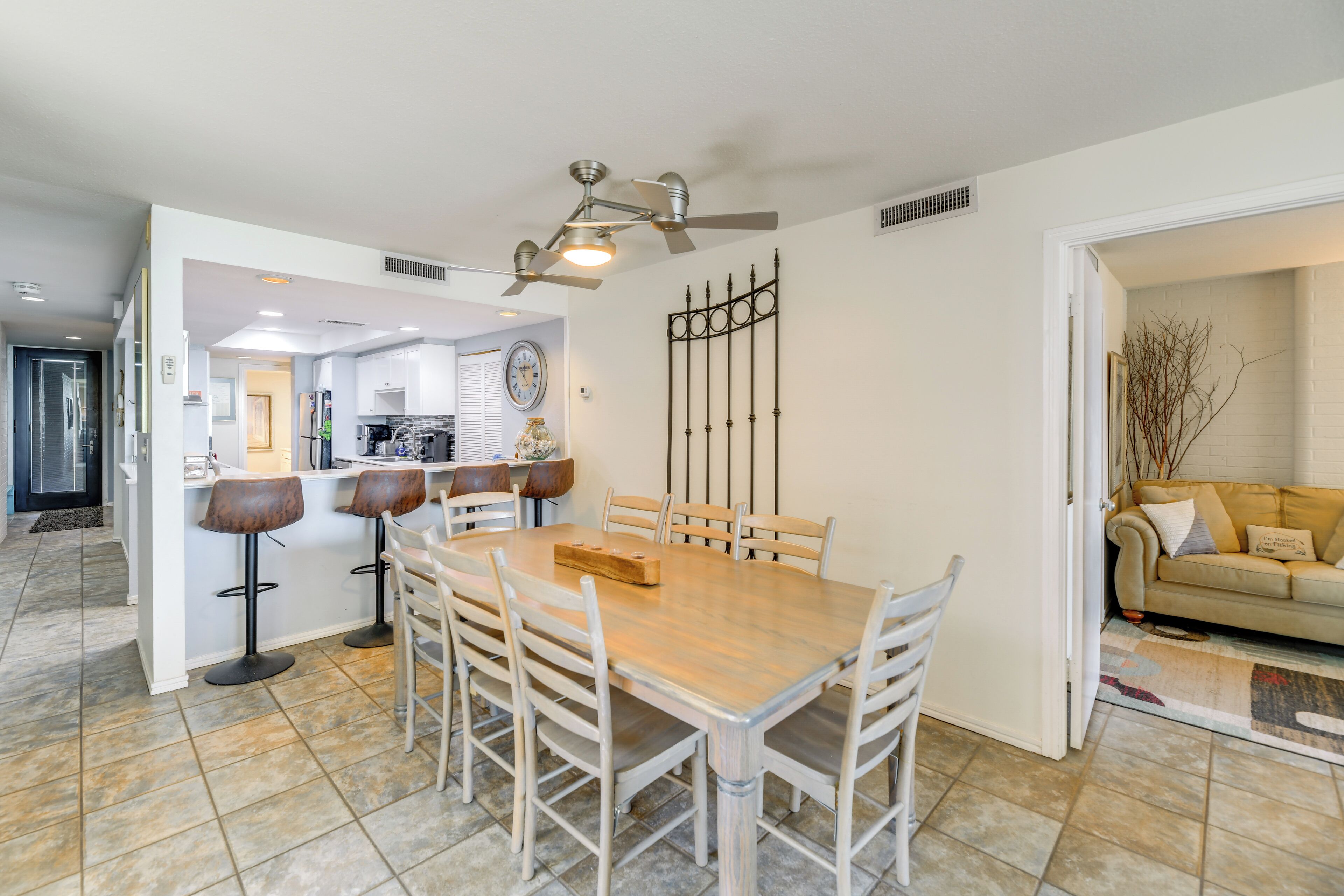 A dining area with a wooden table and chairs, a ceiling fan, and a kitchen in the background.