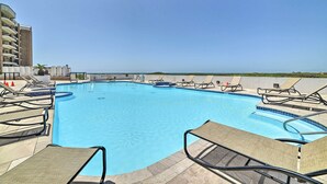 A swimming pool with lounge chairs and a building in the background. - 7th-floor Oceanfront Unit w/ Pools in Port Aransas (Port Aransas)