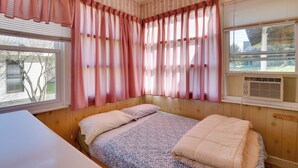 A bedroom with a wooden headboard, a bed with a floral-patterned bedspread, and pink curtains. - Shared Boat Launch: Lake Retreat in Ellenville! (Ellenville)