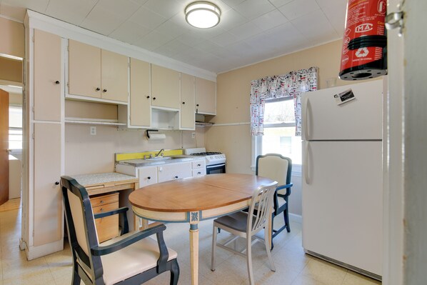 Een kleine keuken met een houten tafel en stoelen, een koelkast en een fornuis.