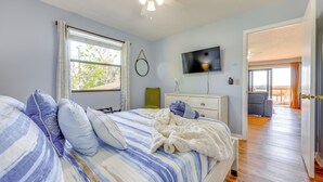 Une chambre avec un lit, un ventilateur de plafond, une télévision et une vue sur l’extérieur.