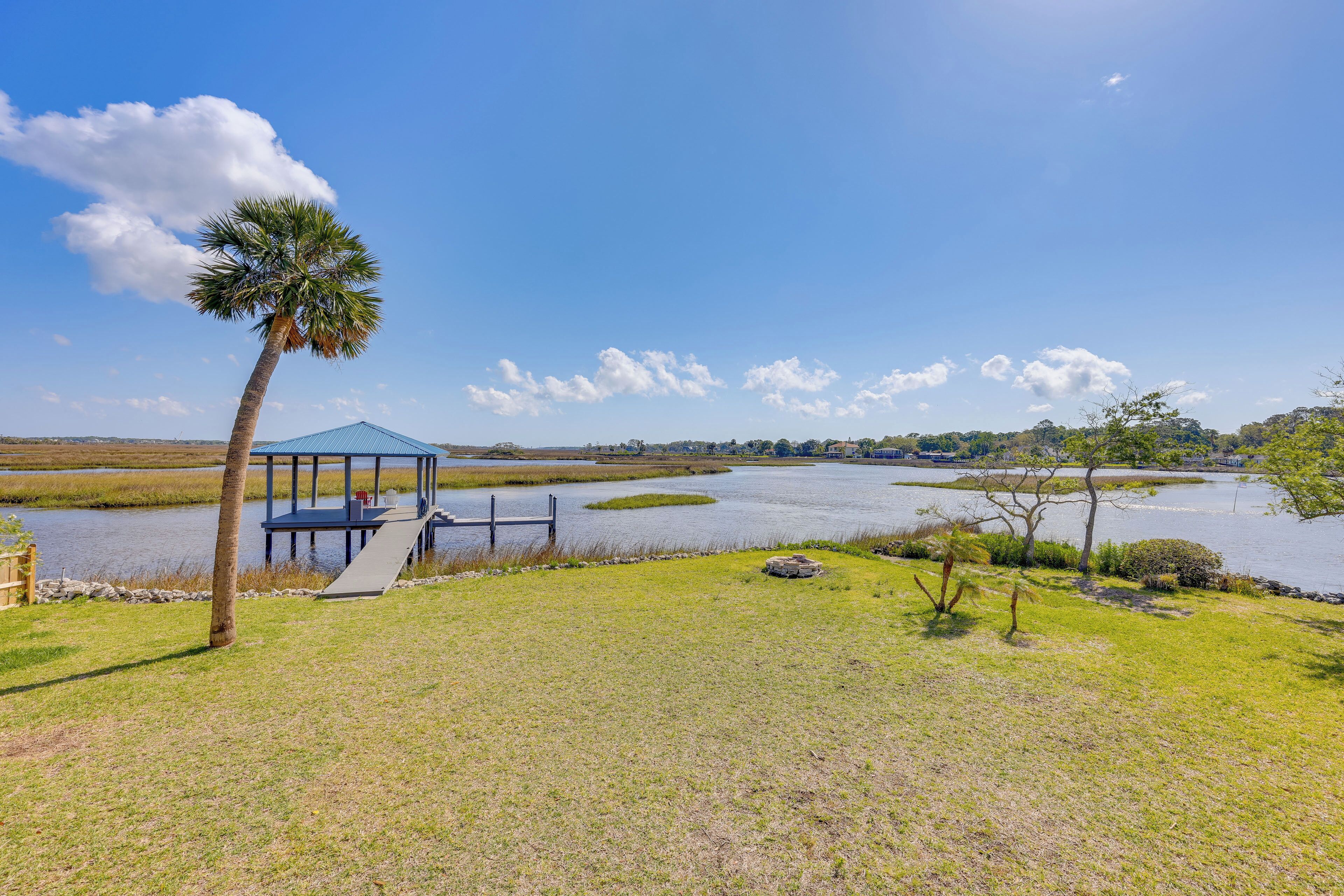 A gazebo by a lake with a palm tree and a dock.