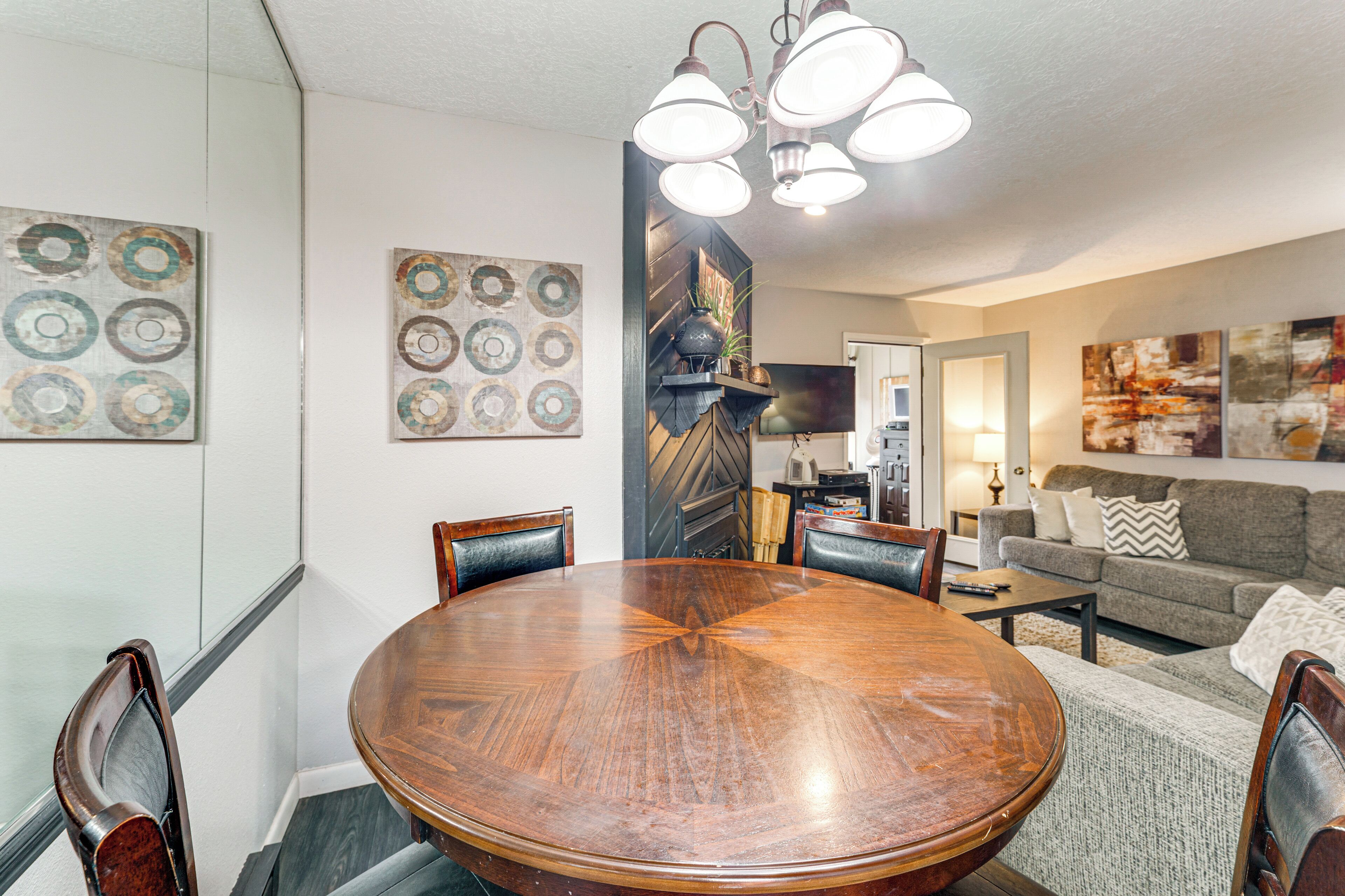 A dining area with a round wooden table and chairs, a sofa, and artwork on the walls.