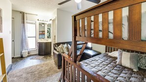Une chambre avec un lit en bois, un ventilateur de plafond et une vue sur la salle de bain.