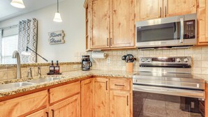 Una cocina con armarios de madera, electrodomésticos de acero inoxidable, encimera de granito e iluminación colgante.