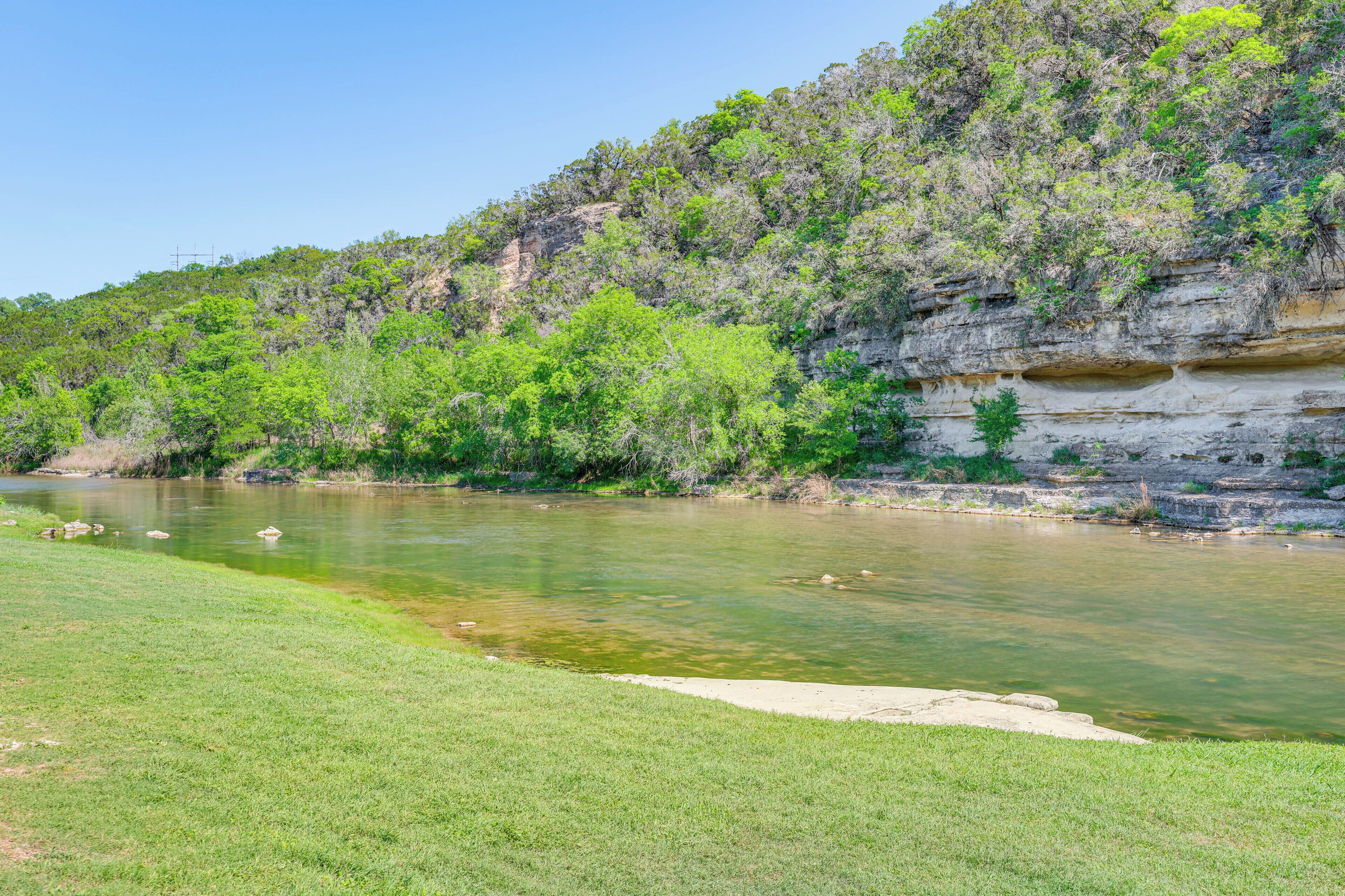 A river with clear water, surrounded by grassy banks and a rocky cliff with sparse vegetation.