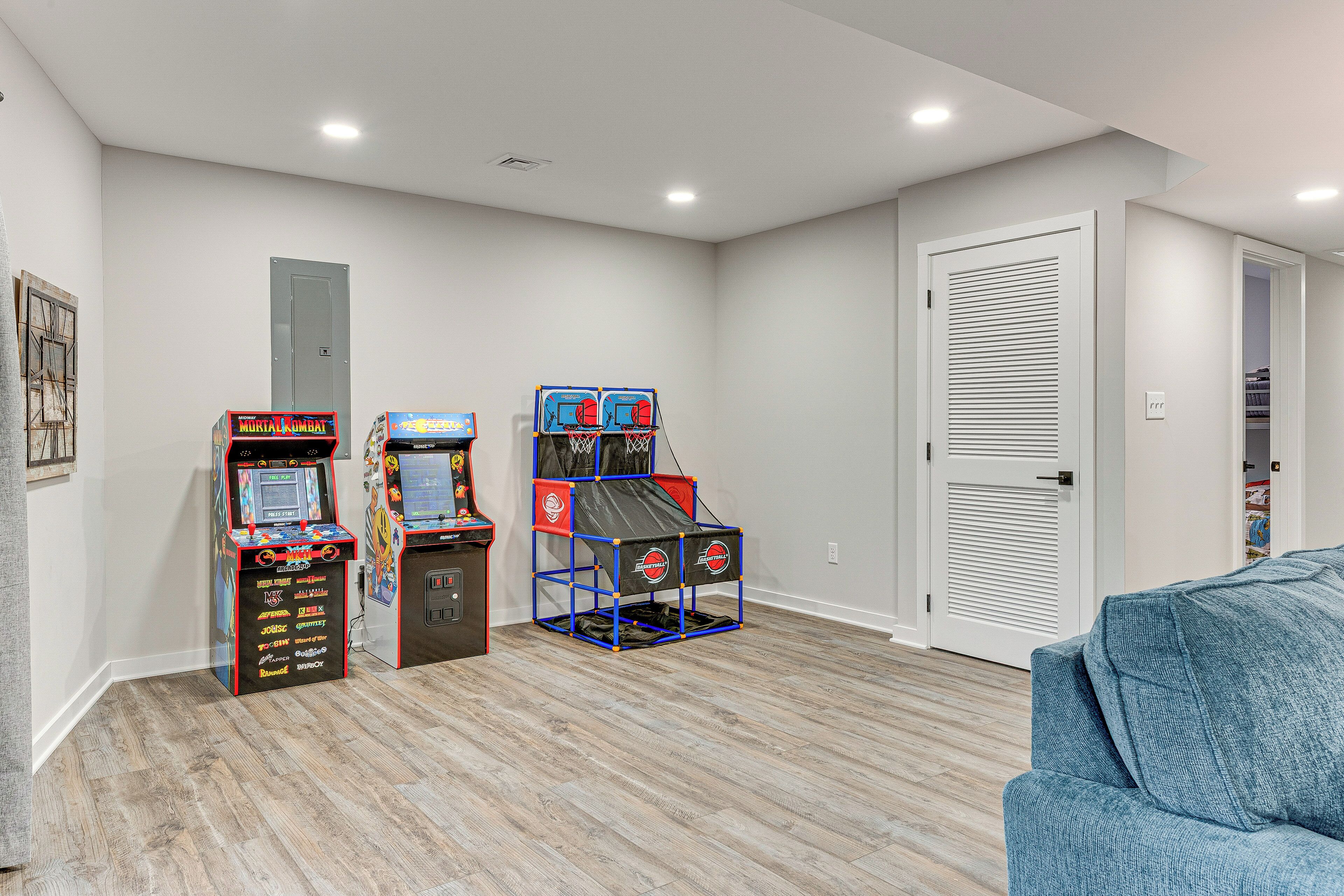 A room with wooden flooring, two arcade machines, a blue couch, and a closed door.