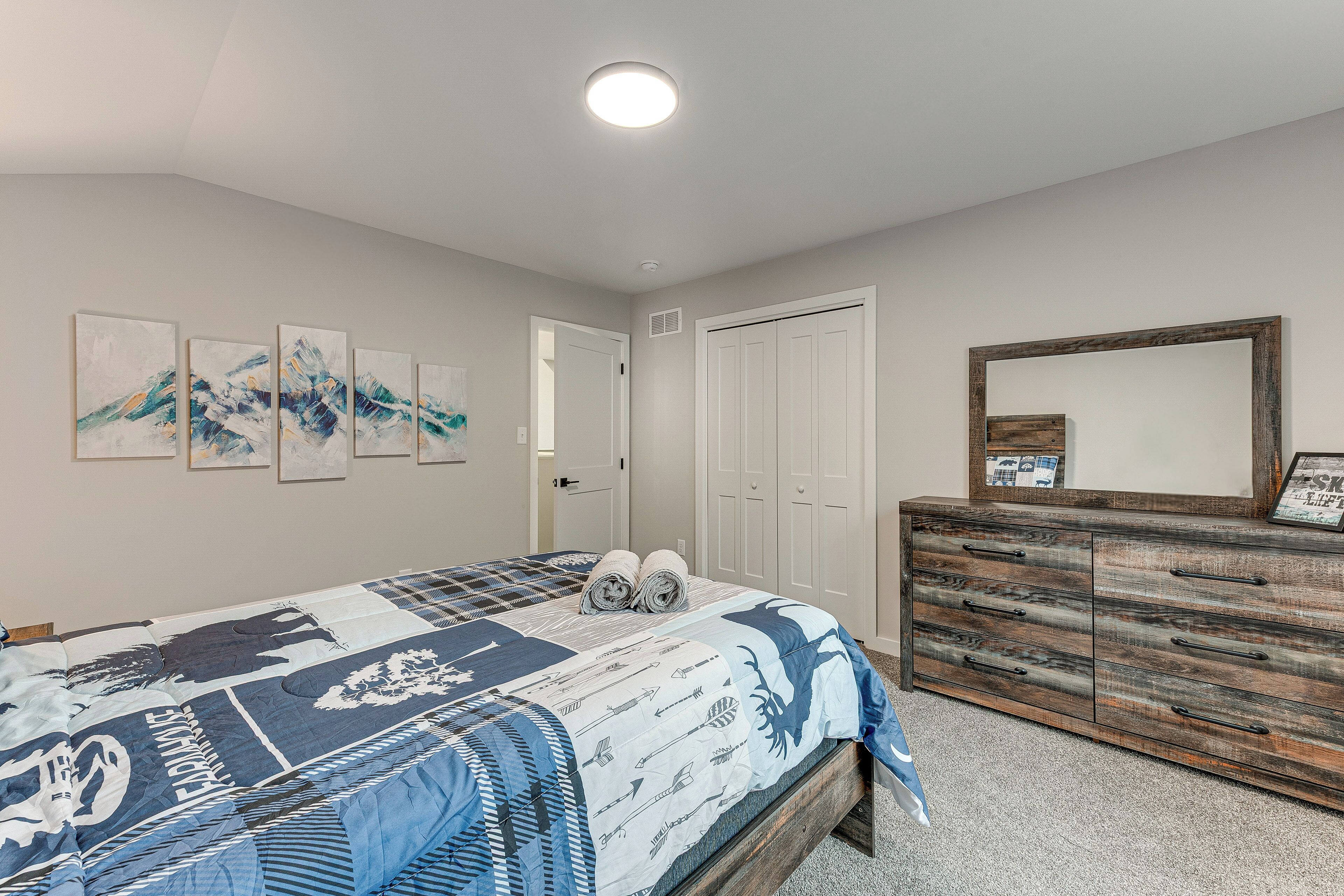 A bedroom with a bed, a dresser, a mirror, and wall art.