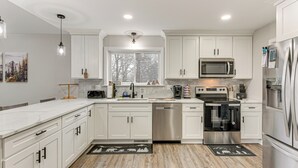 A modern kitchen with white cabinets, stainless steel appliances, and a large window.