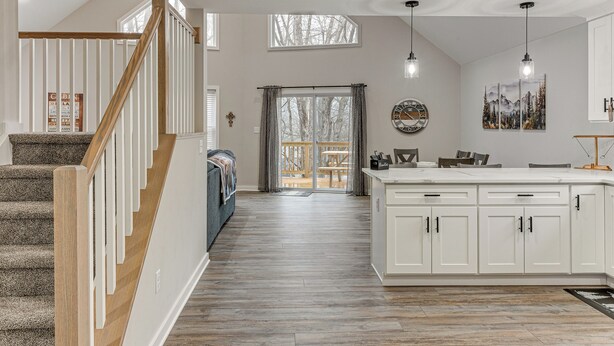 A spacious kitchen with white cabinets, a wooden staircase, and a view to a balcony.