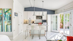 A modern kitchen with white cabinetry, a central island with bar stools, pendant lighting, and a view of the outdoors through large sliding glass doors.