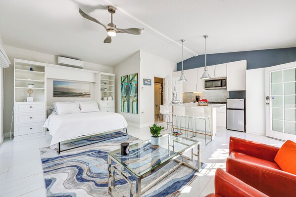 A modern apartment with a bed, a glass coffee table, a red sofa, a kitchen with a microwave, and a ceiling fan.