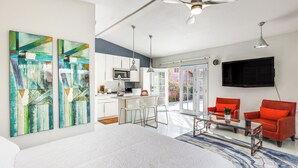 A modern living room with a large bed, a glass coffee table, red chairs, and abstract paintings on the wall.