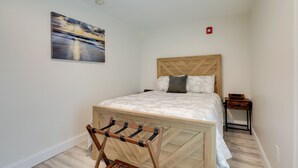 A bedroom with a wooden bed frame, a wooden bedside table, a wall-mounted painting, and a wooden drying rack. - Pet-friendly Wareham Retreat Near Onset Beach! (Wareham)