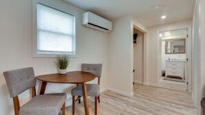 A dining area with a round wooden table, two grey upholstered chairs, a potted plant, and a window with blinds. - Pet-friendly Wareham Retreat Near Onset Beach! (Wareham)