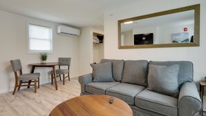 A modern living room with a grey sofa, wooden chairs, a round coffee table, and a large mirror on the wall. - Pet-friendly Wareham Retreat Near Onset Beach! (Wareham)