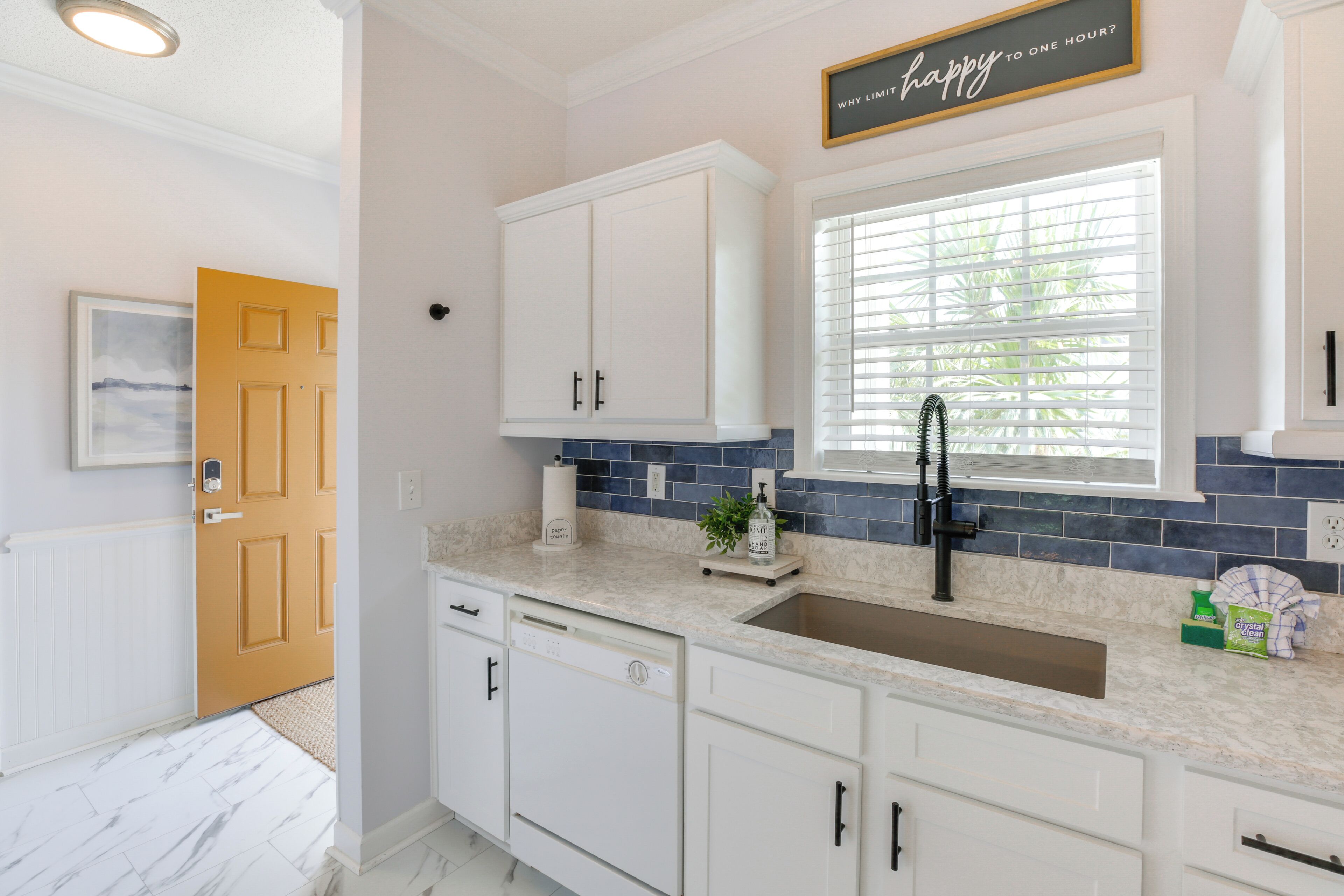 A kitchen with white cabinets, a marble countertop, a sink, and a window with blinds.