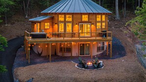 Une cabane en bois dotée d’un balcon, de nombreuses fenêtres et d’un espace aménagé pour faire un feu de camp.