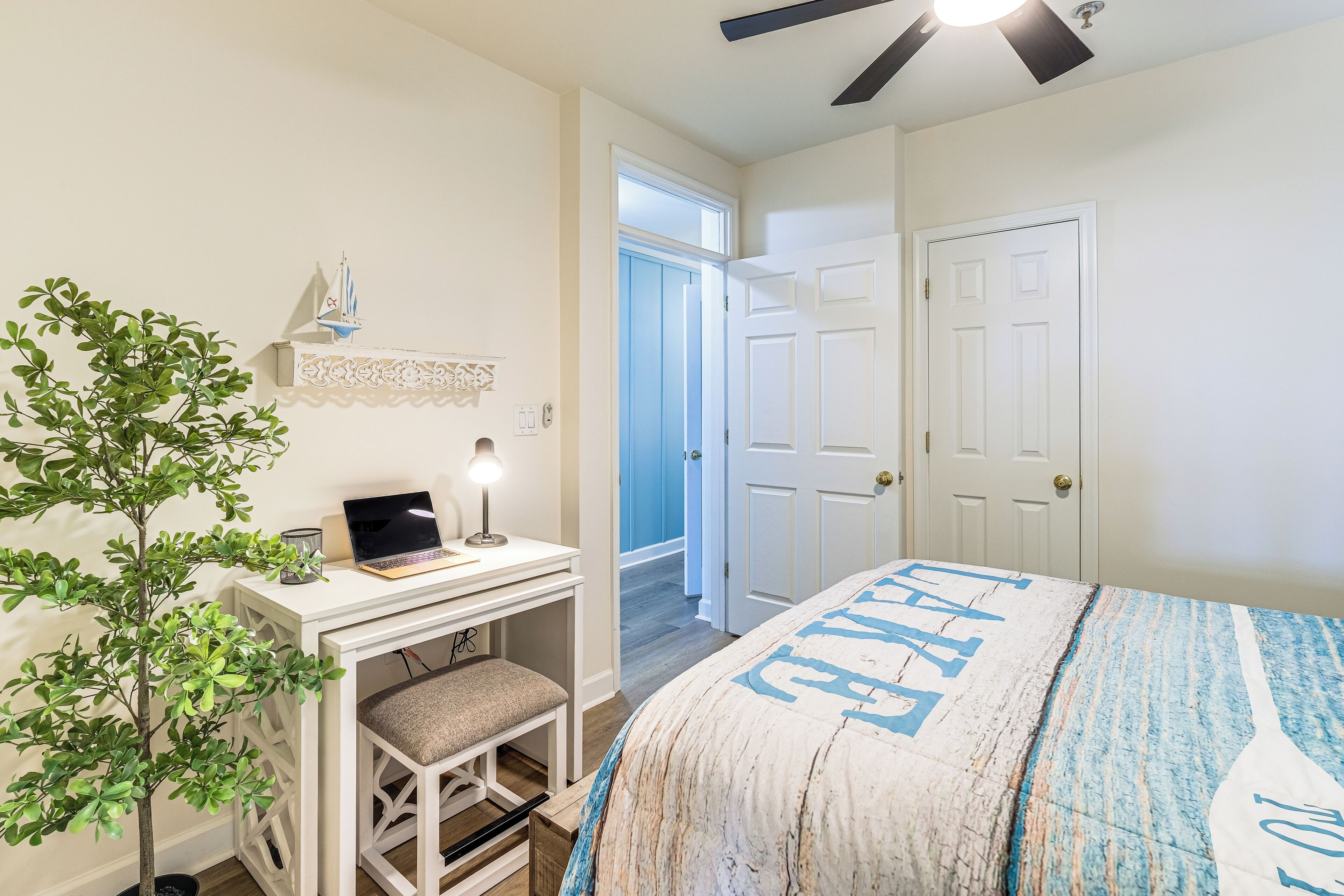 A bedroom with a bed, desk, chair, and a potted plant.