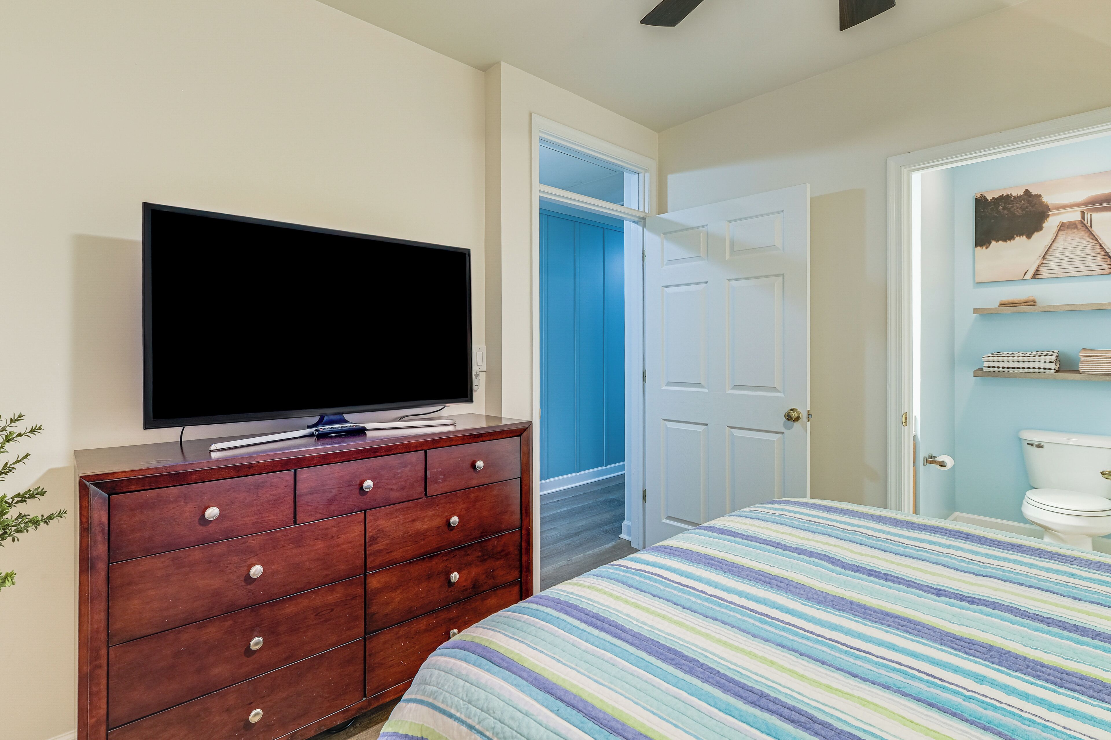 Une chambre à coucher avec un lit, une commode sur laquelle se trouve une télévision, une porte bleue et des toilettes blanches.