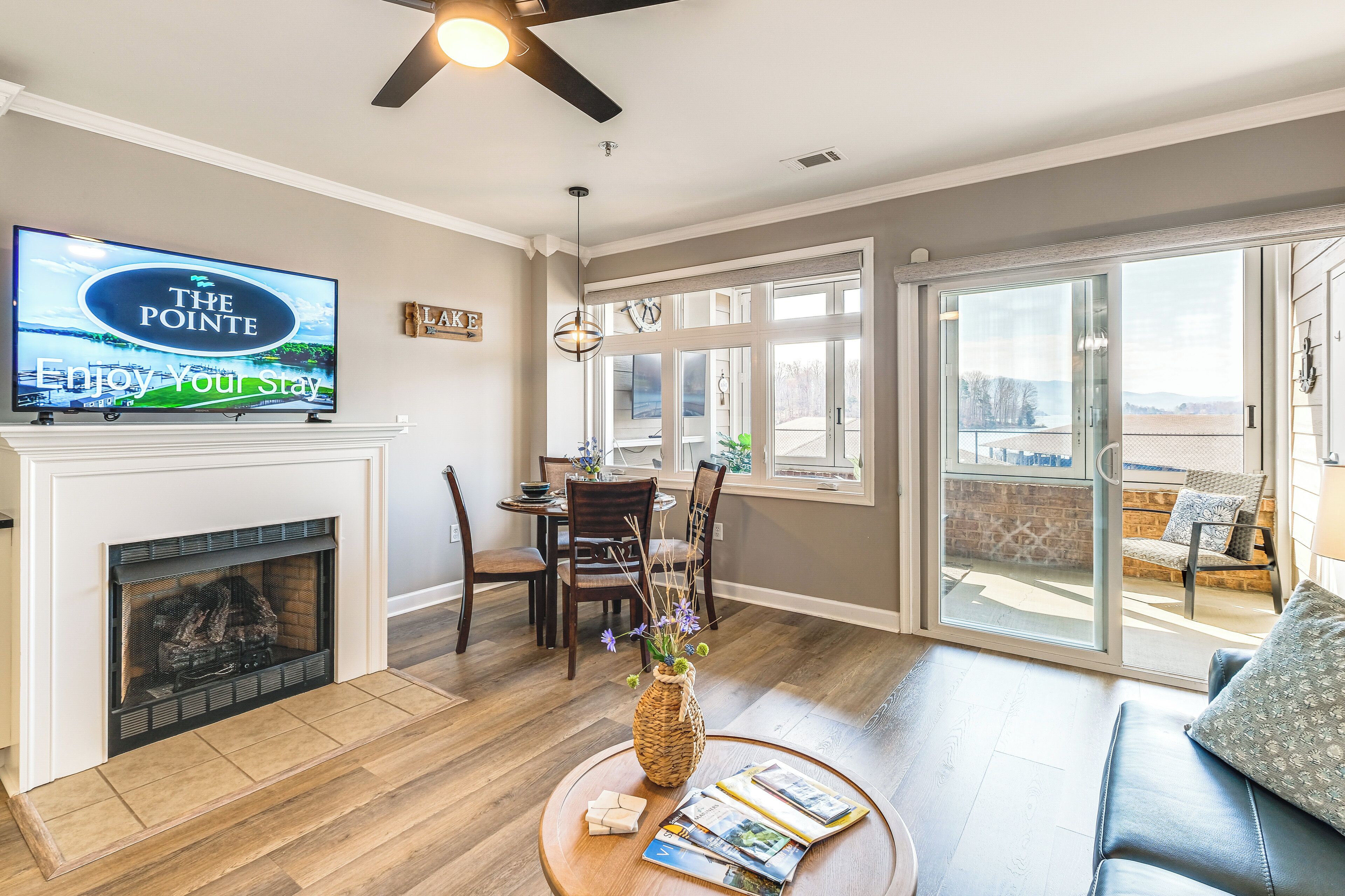 A living room with a fireplace, a television, a dining area, and a balcony with a view.