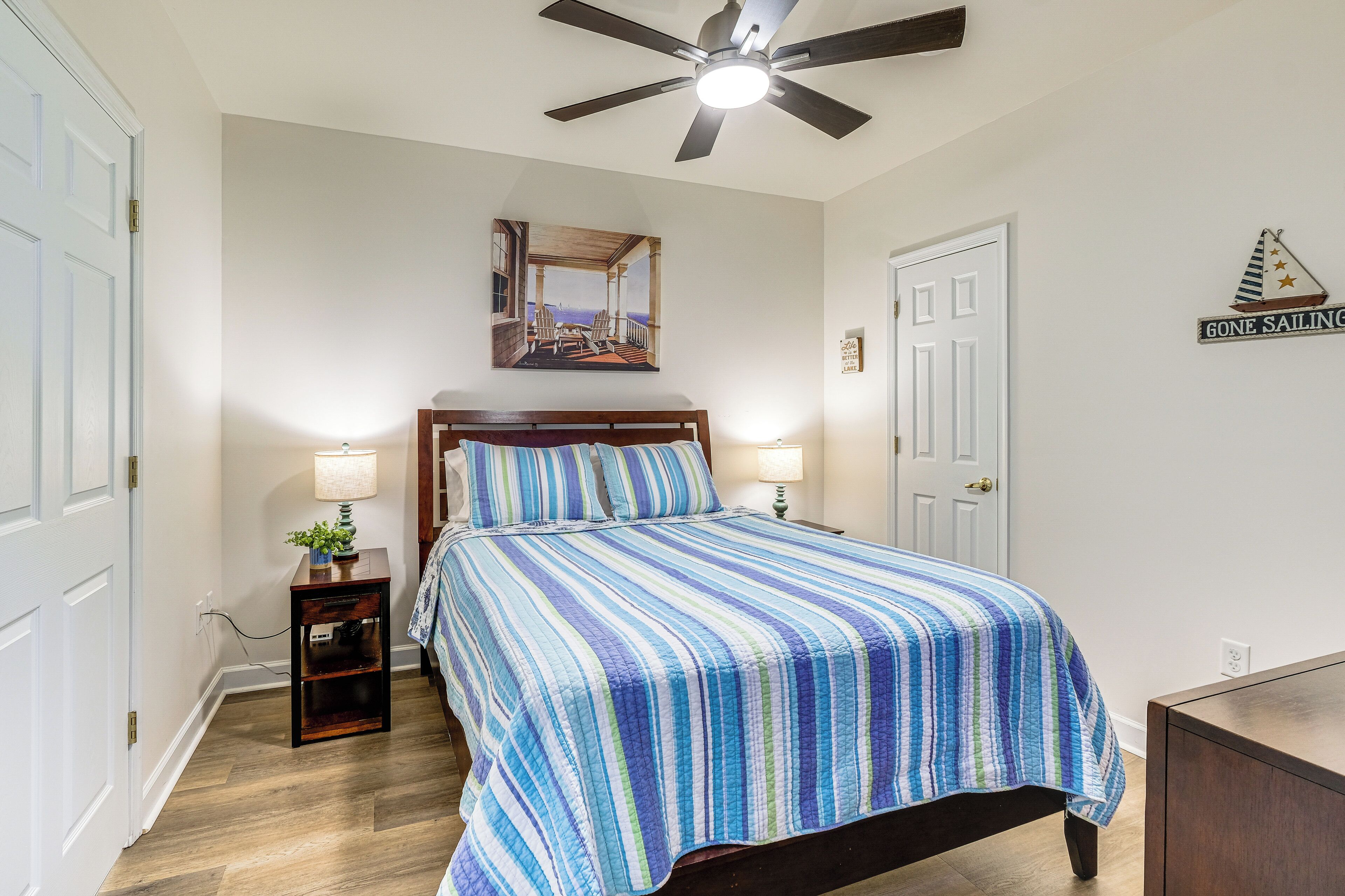 A bedroom with a bed, a nightstand, a ceiling fan, and a wall-mounted mirror.